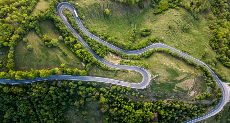 Vue aérienne d’une route sinueuse en montagne entourée de verdure, évoquant l’utilisation du Pegasus TRK Evo dans les relevés d’infrastructure routière, entre autres pour évaluer la préconstruction, surveiller l’avancement des travaux et analyser l’état de la chaussée.